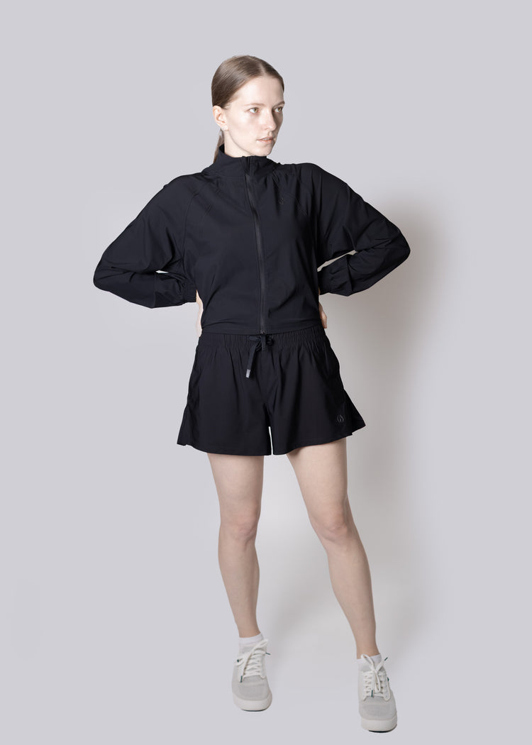 A girl wearing a black outfit with a jacket and shorts on a plain background