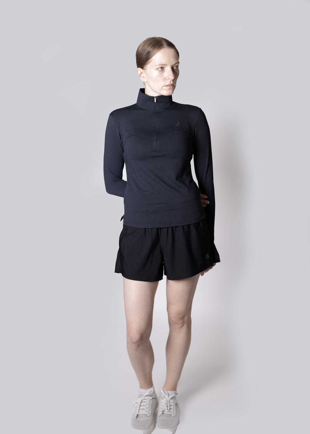 A girl wearing a black long-sleeve top and black shorts on a light gray background