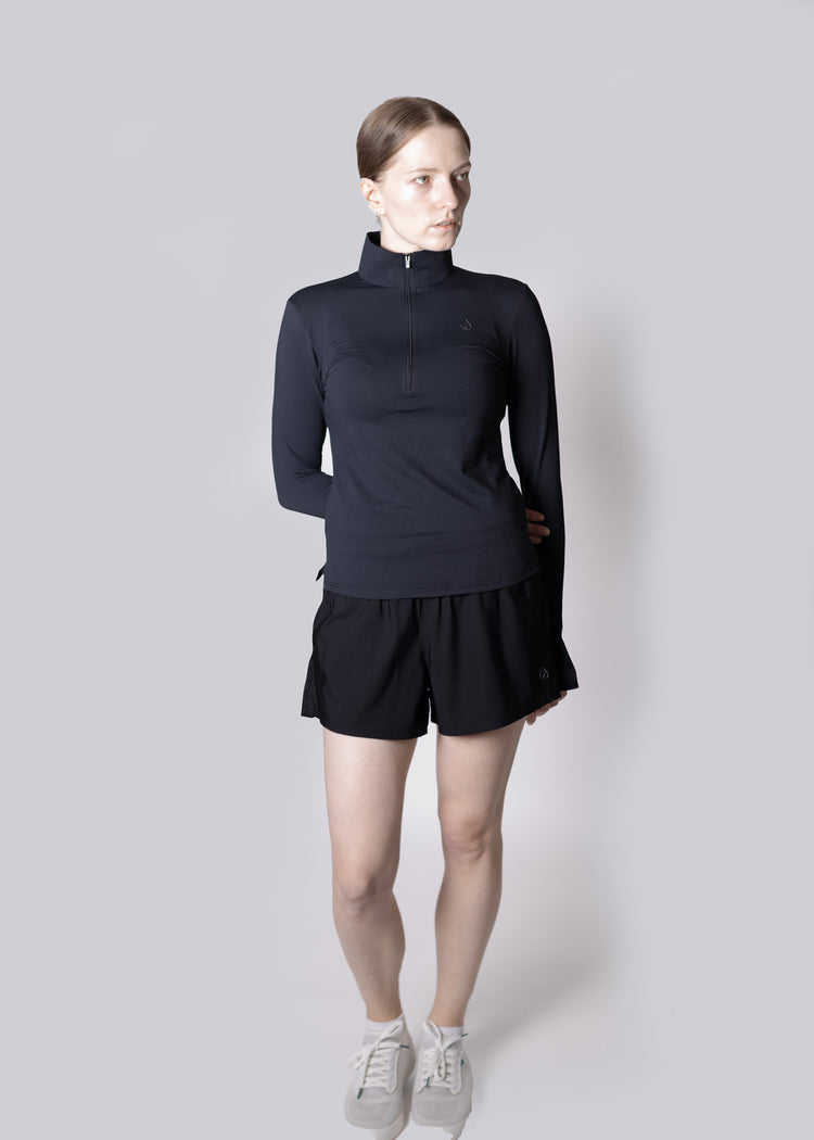 A girl wearing a black long-sleeve top and black shorts on a light gray background