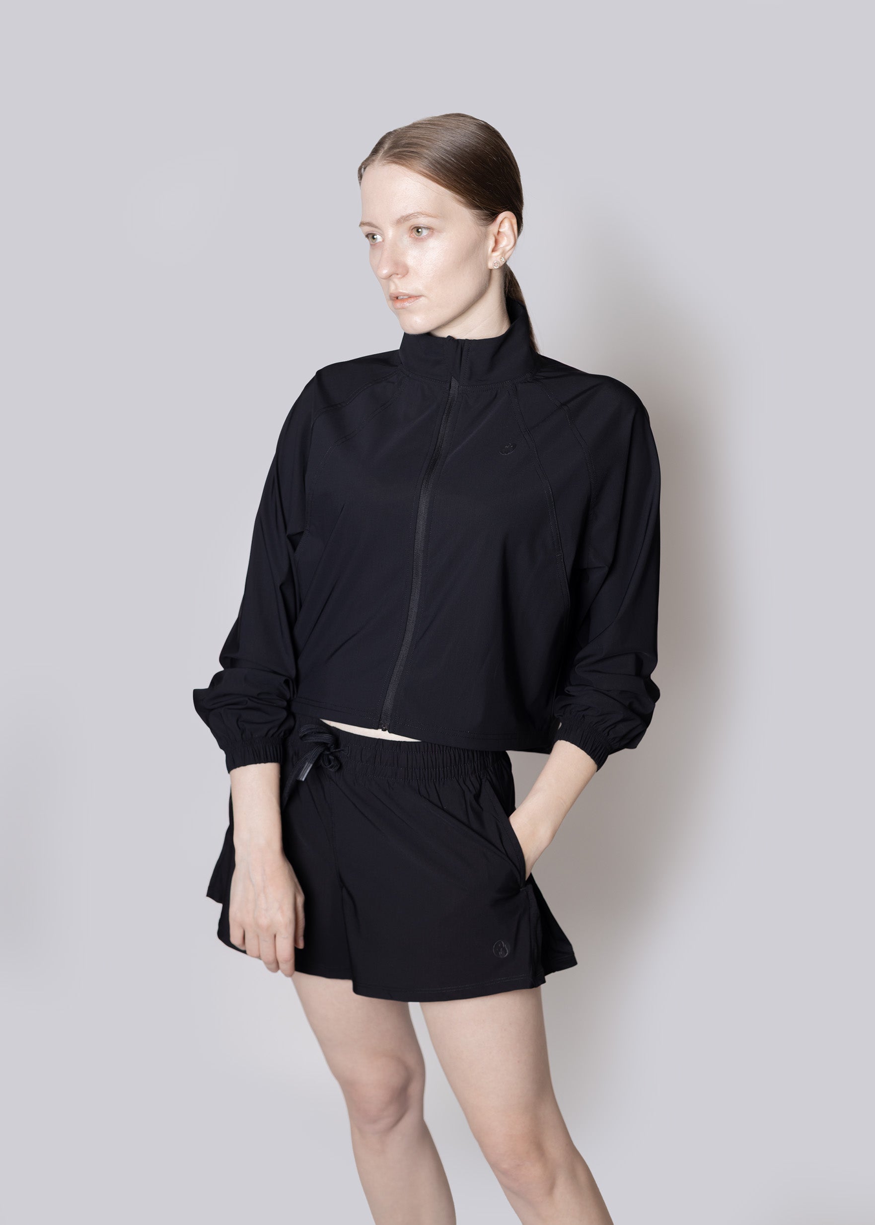 A woman wearing a black outfit against a plain background, Jacket and Shorts