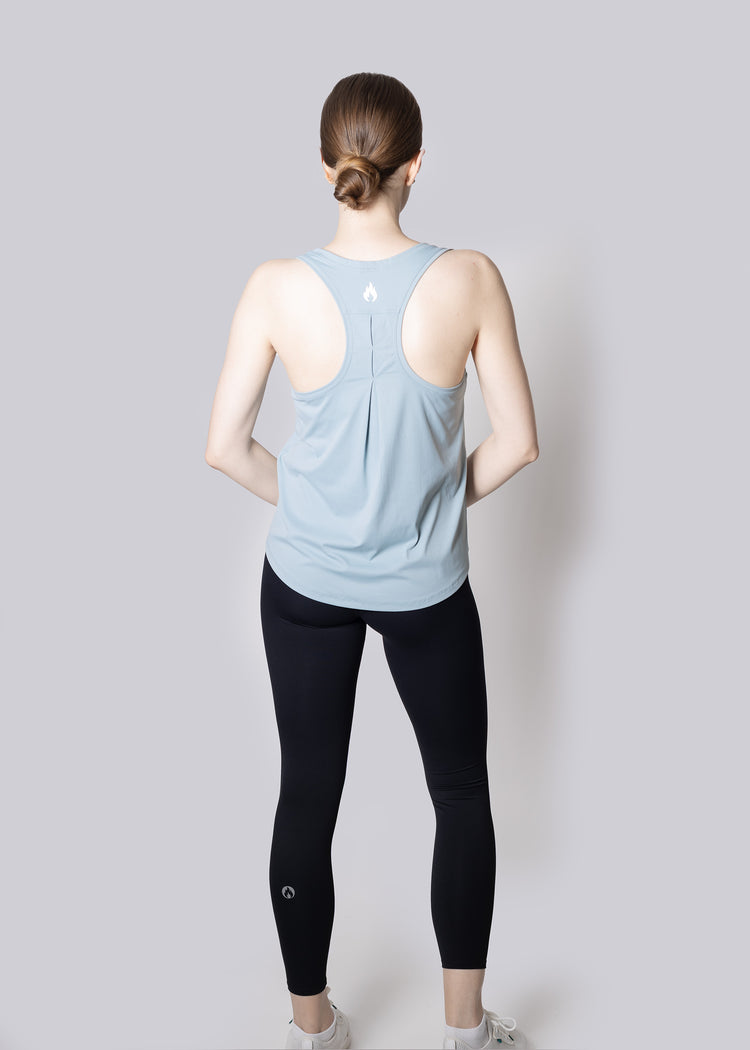 A girl wearing a light blue tank top and black leggings on a plain background