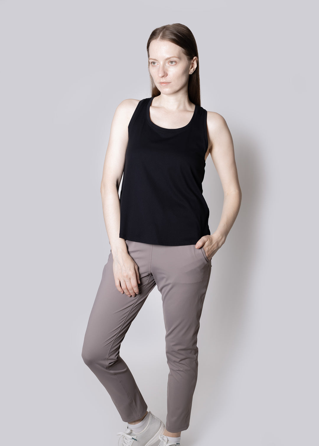 Woman wearing a black tank top and gray pants against a light gray background