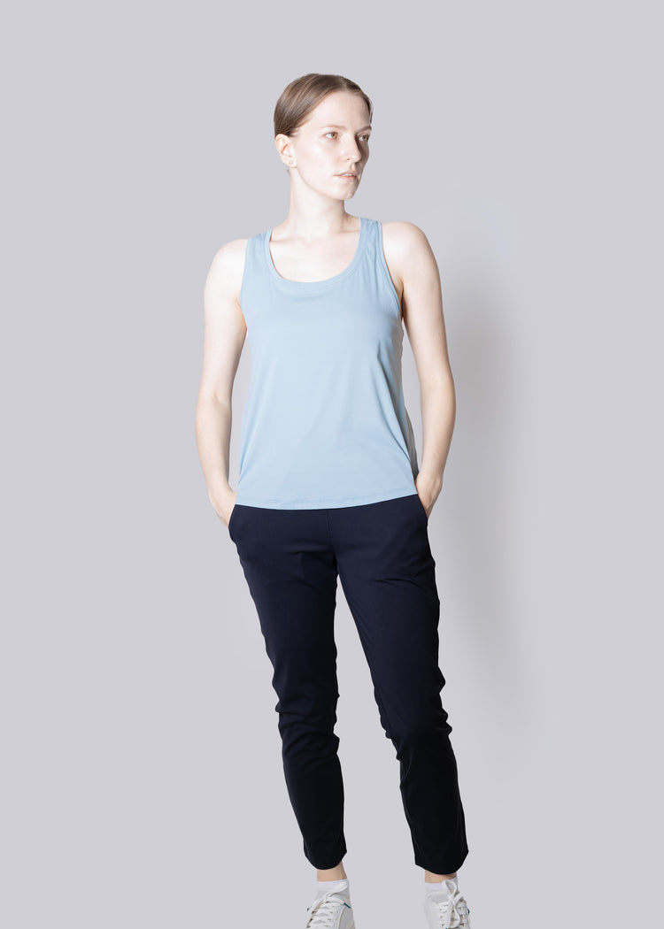 A girl wearing a light blue tank top and black pants on a plain background