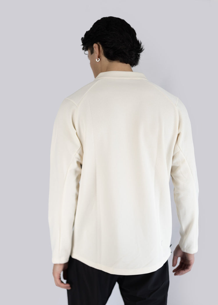 A model wearing a cream-colored shirt with long sleeves on a gray background